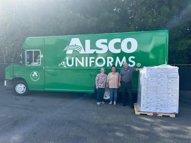Alsco Uniforms employees standing next to a green delivery truck and a pallet of first aid kits.