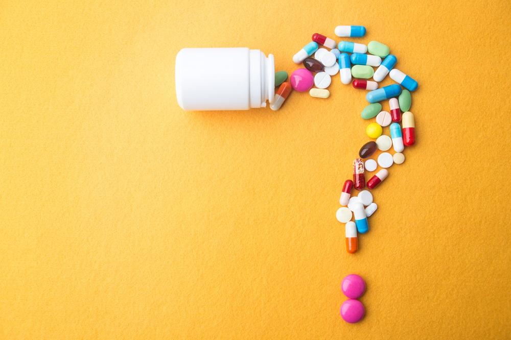 A question mark made out of various pills spilling out of a bottle.