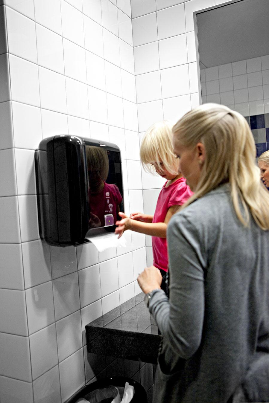 People using an automatic paper towel dispenser in a bathroom