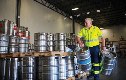 Worker in hi-vis safety vest moving metallic food and drink barrels