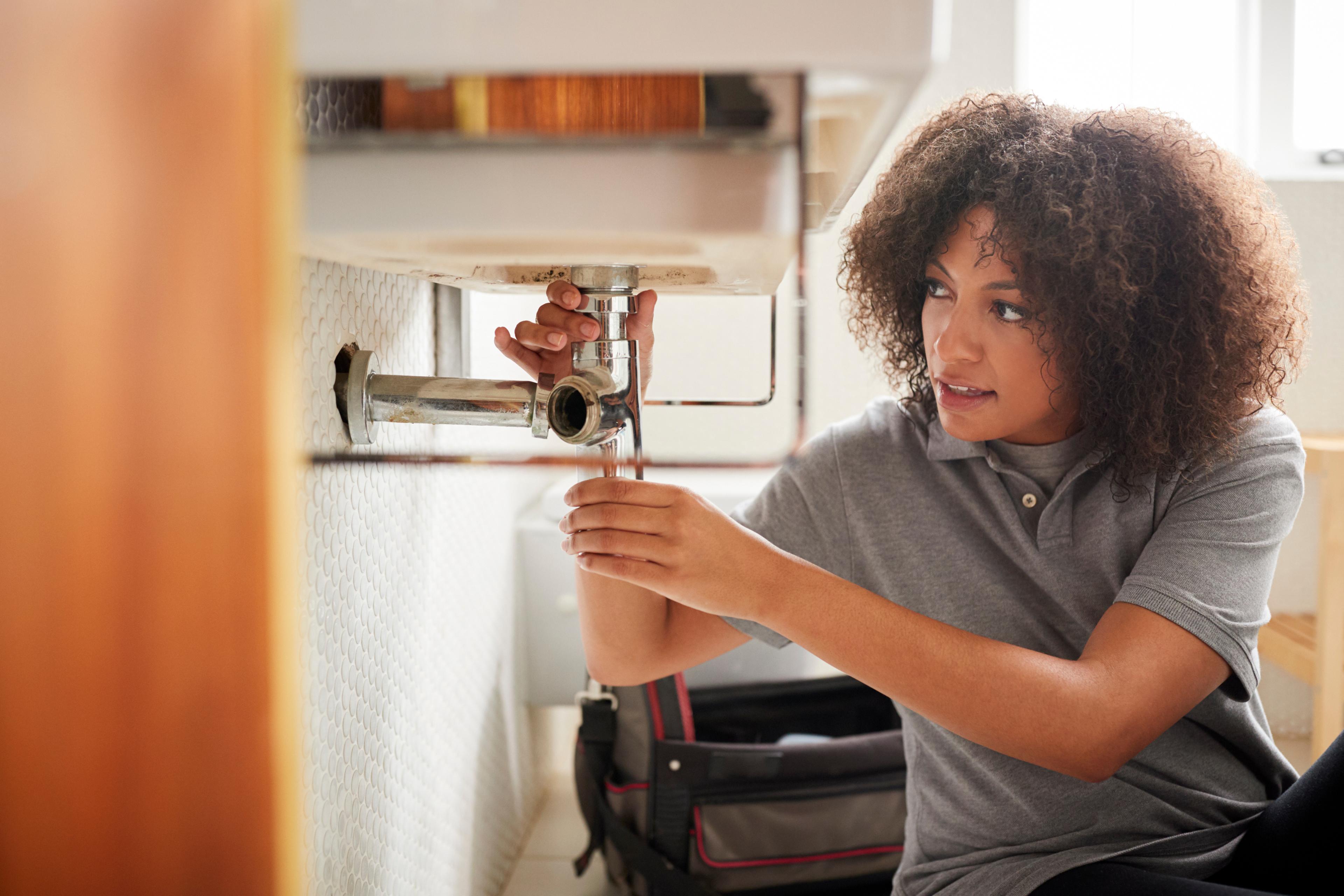 Woman fixing plumbing under a sink